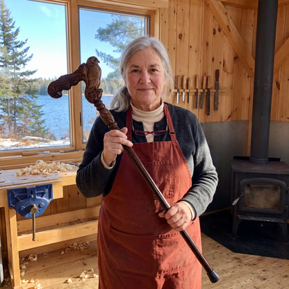 Odette Thibodeau holding a finished owl-head cane in her workshop by the lake