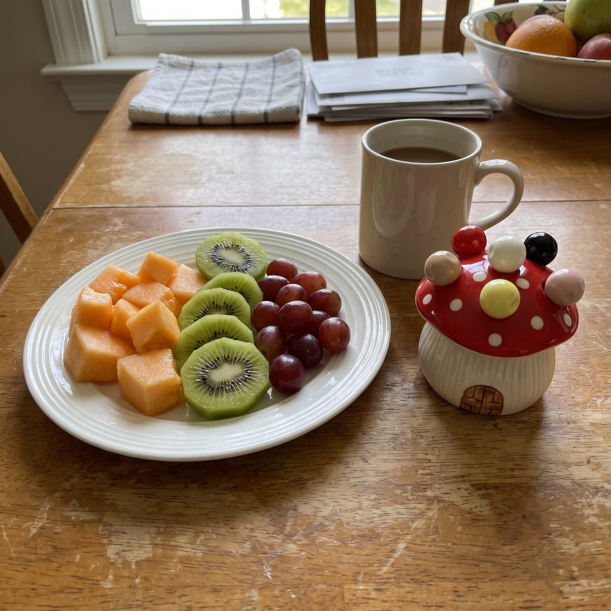 Red mushroom fork house next to a plate of melon, kiwi and grapes