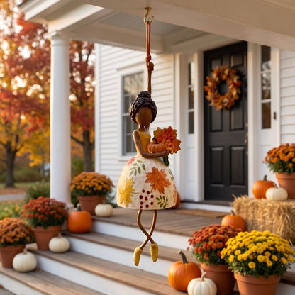 The Harvest Dancer hanging above front porch steps with pumpkins and mums